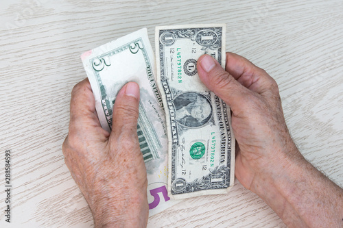 Hands of an elderly woman close up holding 1 and 5 dollars.