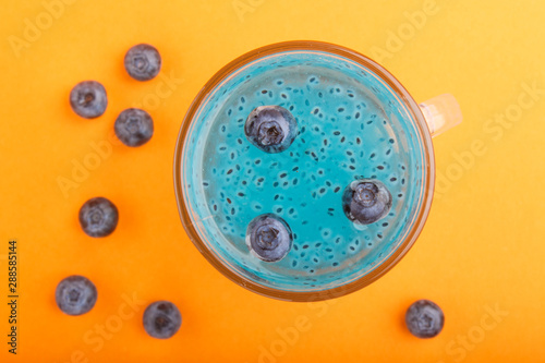 Glass of blueberry blue colored drink with basil seeds on orange background. Morninig, spring, healthy drink concept. Top view photo