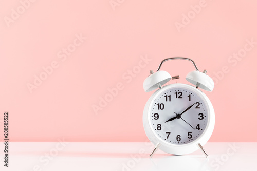 White alarm clock on pastel pink background. Trendy minimalist style. copy space