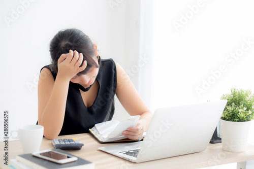 Beautiful young asian woman calculating expenses household and writing notebook on desk, girl checking bill and stress and note, female worry debt and tax, finance and business concept.