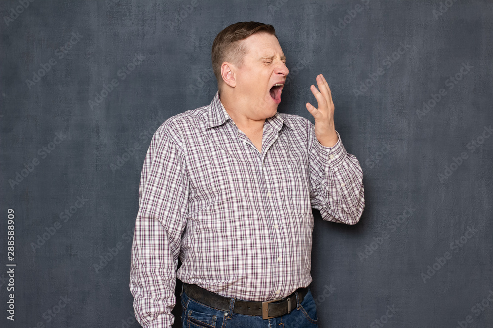 Portrait of man raising hand to cover mouth while yawning