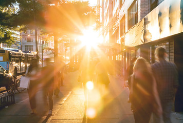 Groups of busy people walking down the crowded sidewalks of 14th Street in New York City with the summer sunset shining bright