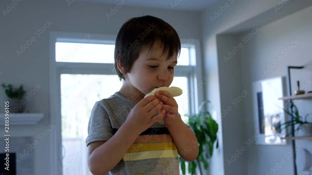 Toddler boy eating banana in kitchen - wide shot - slow motion Toddler boy eating banana in kitchen - wide shot - slow motion