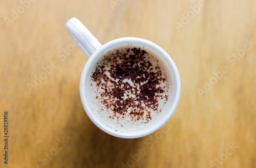 Coffee with foam and chocolate mug in a white mug on a wooden table. Cappuccino in a white mug on a light background. Good morning. Morning cappuccino for breakfast. Coffee in a mug top view. 