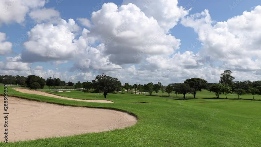 Landscape of large golf course showing green grass and sandpits and trees in the distance of the golf course. Lots of clouds in the blue sky. Landscape of large golf course showing green grass and sandpits and trees in the distance of the golf course. Lots of clouds in the blue sky.
