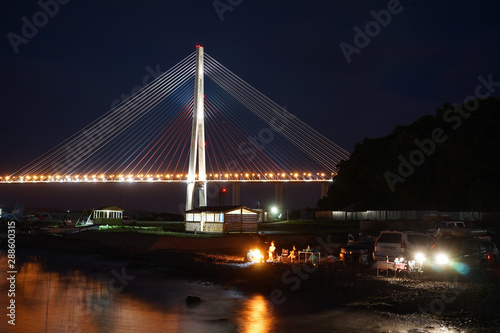 Night landscape with views of the Russian bridge. People relax on the beach.