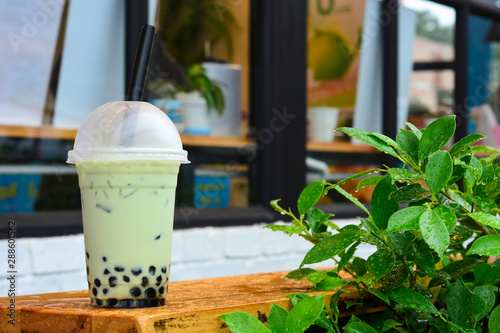 glass of milk bubble matcha green tea with tapioca pearls on wooden table with green leaves on blurred cafe restaurant background photo