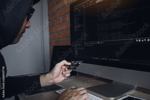 Hacker in the hood working with computer and holding credit card with payment hacking concept.