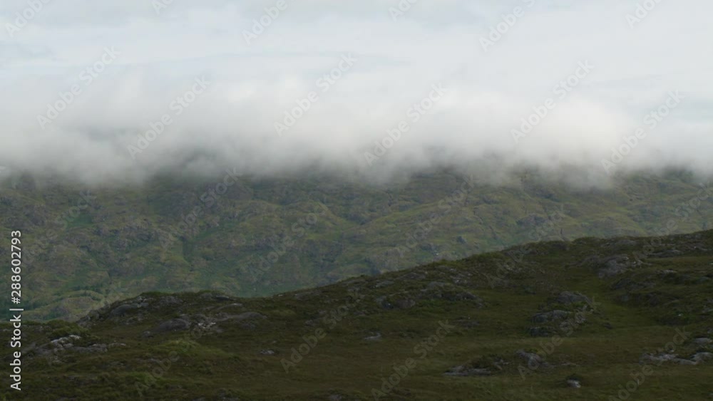 Steady, medium wide shot of green plains and hills hidden by thick fogs and clouds.