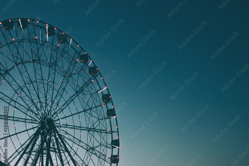 Glowing lights on Ferris wheel, resort nightlife, background, beautiful sky. High iso, grain Glowing lights on Ferris wheel, resort nightlife, background, beautiful sky. High iso, grain