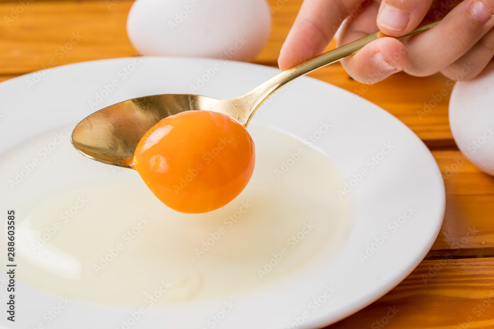 白いお皿に生卵の黄身がスプーンから落ちる瞬間、料理
