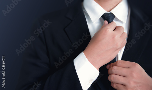 Businessman in black suit and adjusting necktie.