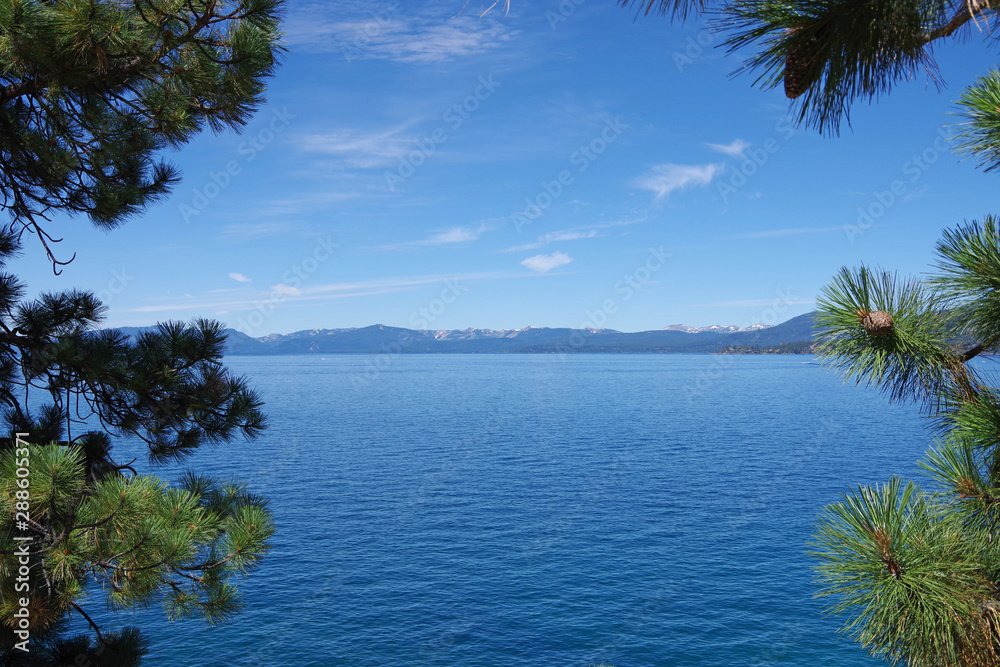 A panoramic view of blue lake Tahoe forest mountains in the background and a blue sky with a few little clouds on a bright summer day
