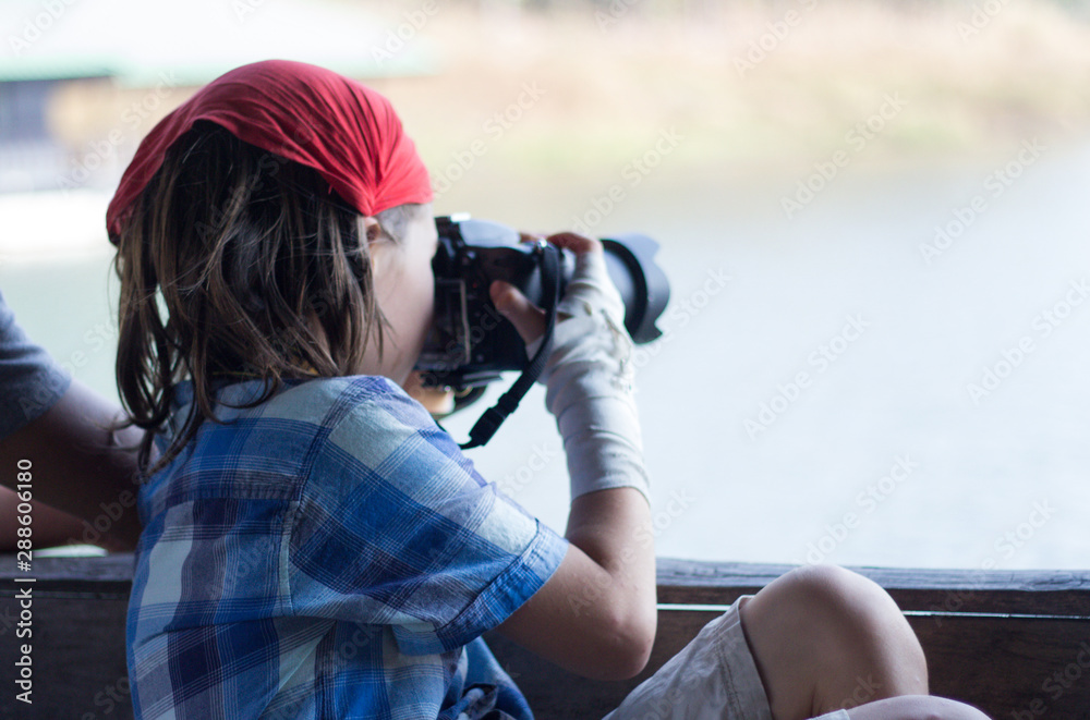 The boy holding the camera is shooting lake view. The boy holding the camera is shooting lake view.