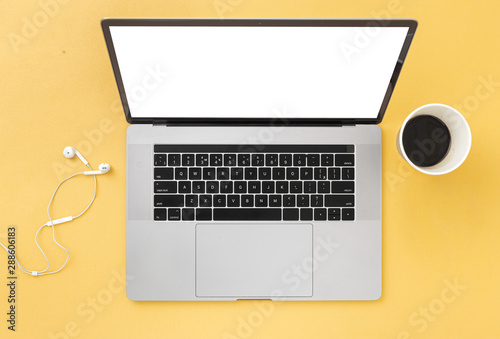 Creative office desktop Laptop with blank screen on a yellow background with coffee and headphones