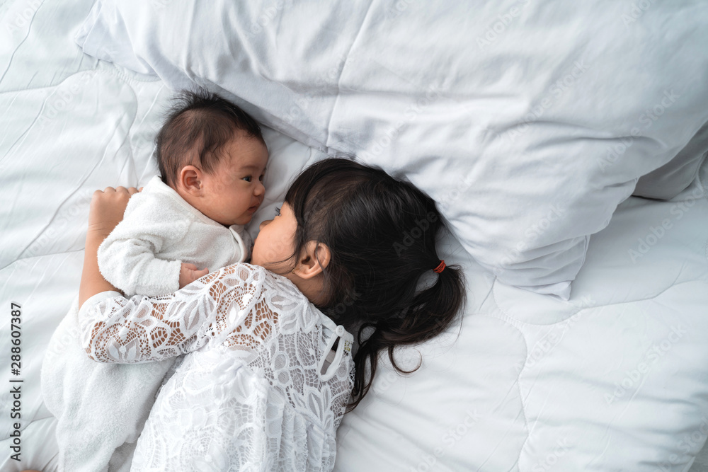 asian daughter kid with infant sibling playing on bed wearing white together asian daughter kid with infant sibling playing on bed wearing white together