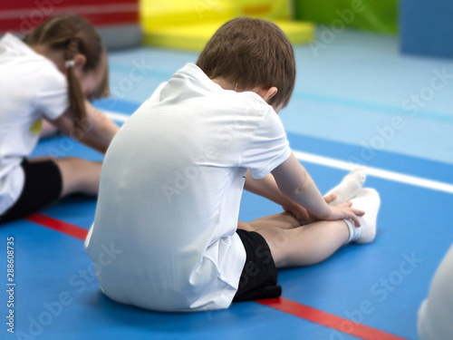 The boy is engaged in acrobatics. A child dressed in a white t-shirt is doing exercises.