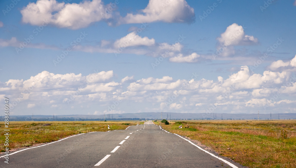Empty asphalt road to the horizon through autumn steppe under blue sky with clouds at Khakassia, Siberia, Russia.