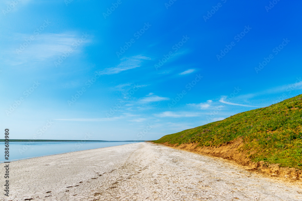 The green grassy hill on the coast of the salt lake and wide stripe of the dry cracked soil. Gruzskoe lake, Rostov-on-Don region, Russia