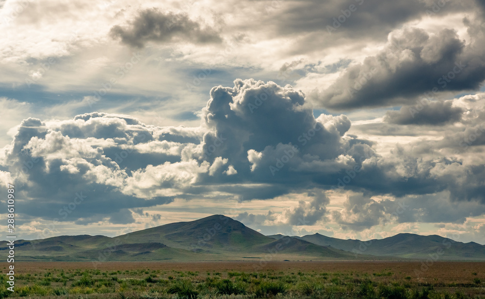 Obraz premium Grass hills on horizon in steppe under heavy clouds sky during sunset with sun light beams at Khakassia, Siberia, Russia.