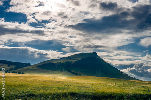 Grass hills covered with trees in steppe under spectacular clouds sky during sunset at Khakassia  Siberia  Russia.
