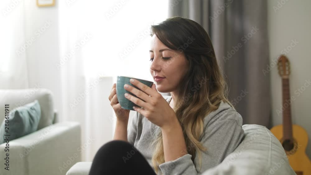 Young girl drinks tea from a large cup in the living room in the morning Young girl drinks tea from a large cup in the living room in the morning