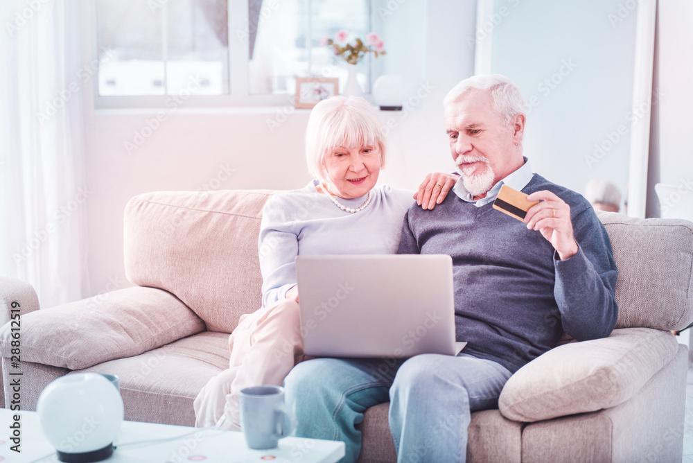 Bearded elderly man holding bank card shopping online with wife