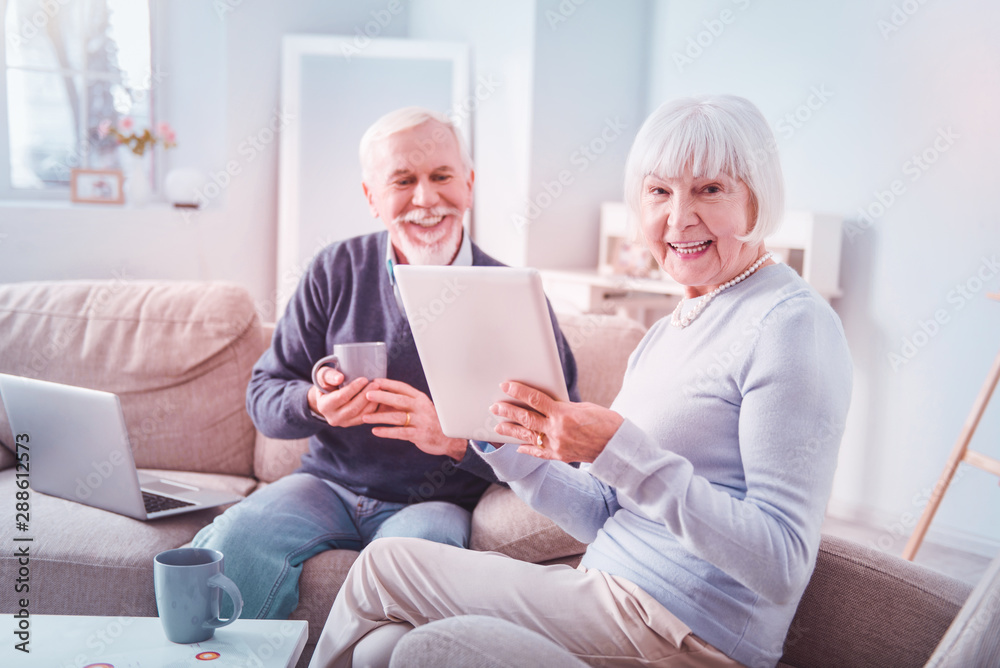 Beaming elegant retired woman wearing blue sweater holding tablet Beaming elegant retired woman wearing blue sweater holding tablet