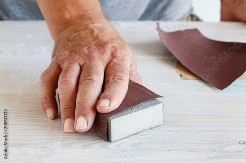 Man uses a sandpaper to restore wooden surface.