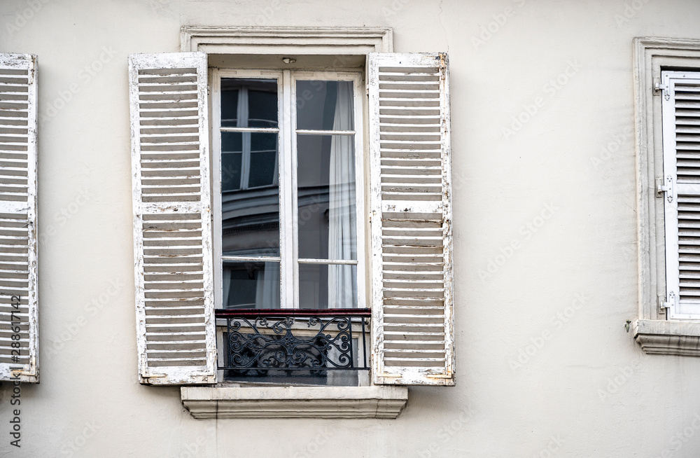 Window with the rickety shutters of an old stone multi-storey residential building