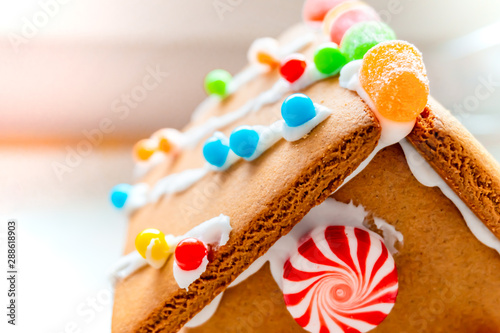 Cute, child-made gingerbread house, with imperfections (a real gingerbread house assembly), for the Christmas holiday season, as a decoration. Classic holiday activity and dessert.