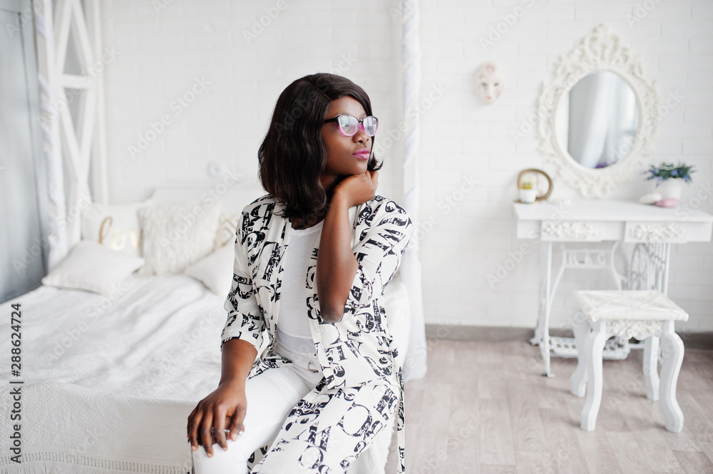 Pretty african american woman in eyeglasses, black and white dress posed in room.