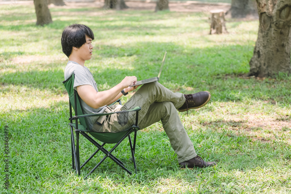 man sitting on camping chair and working with laptop computer in the garden man sitting on camping chair and working with laptop computer in the garden