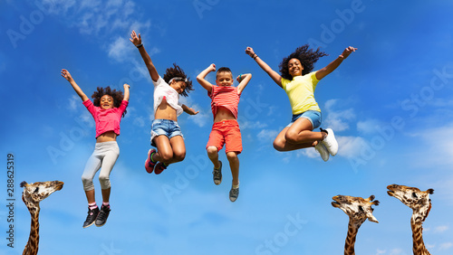 Happy kids group jump higher than head of giraffes