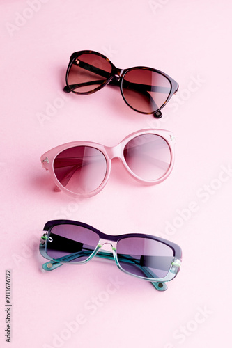 Collection of fashionable sunglasses on pink background. Sunglasses of different shapes and colors flat lay