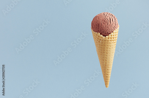 Chocolate ice cream in crisp waffle cone on pastel blue background, mock up for design, summer food.