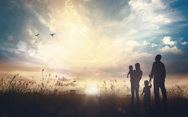 Silhouette of a christian family with children looking at the sunrise with birds flying, concept of hope, faith and new beginning