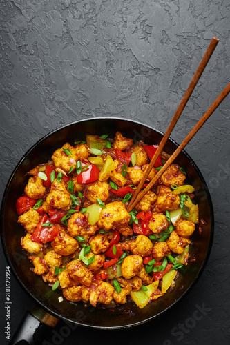 Gobi Manchurian in pan at black concrete background. Gobi Manchurian is Indian Chinese cuisine dish with cauliflower, tomatoes, onion, soy sauce. Copy space