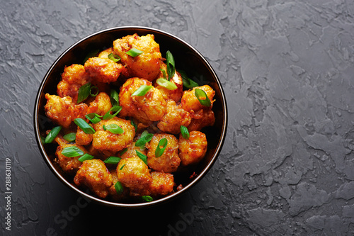 Gobi Manchurian in bowl at black concrete background. Gobi Manchurian is Indian Chinese cuisine dish with cauliflower, tomatoes, onion, soy sauce. Copy space