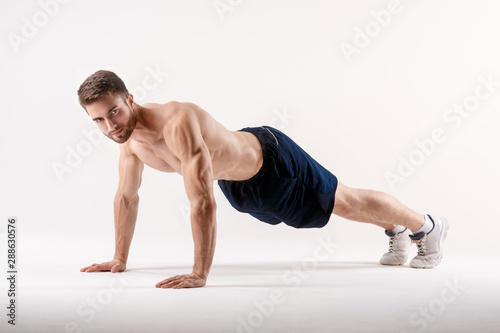 young man with a beard of a sports physique doing push-ups from the floor on a white isolated background, sportsman goes in for sports