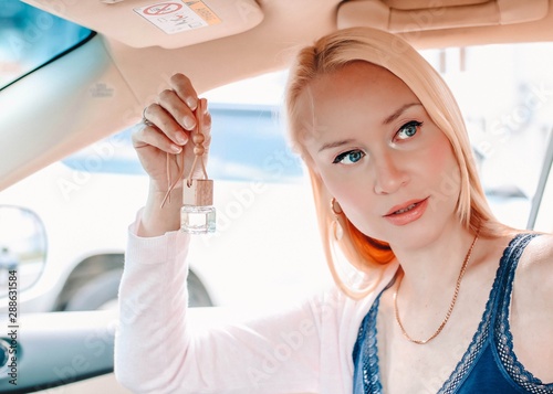 Beautiful blonde hangs car perfume on the rear view mirror in the car.