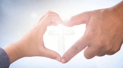 Child and adult hands forming heart shape around christian cross with bright light background