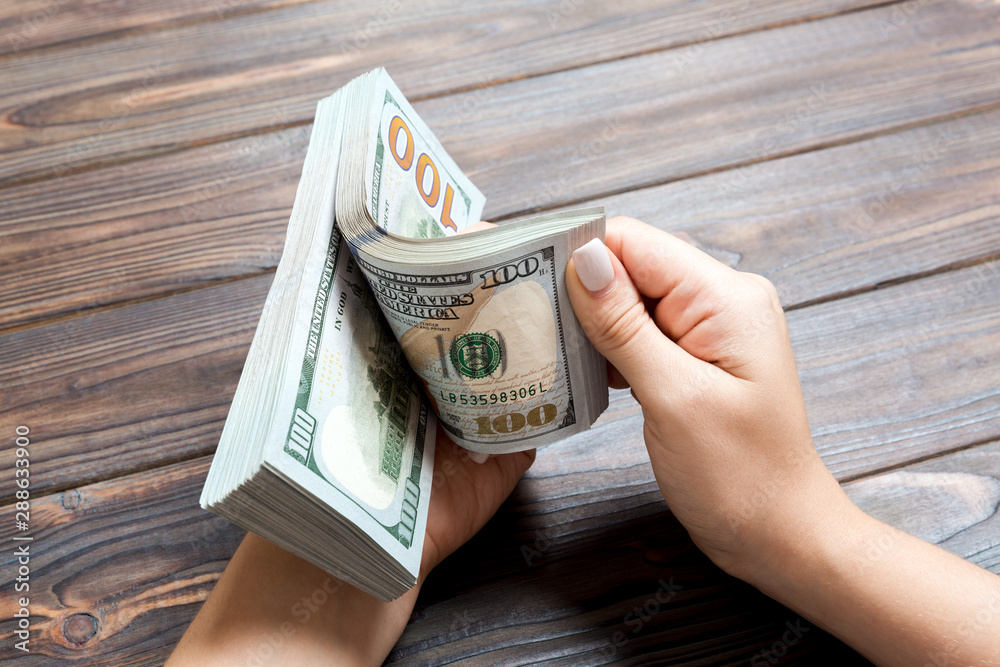 Perspective view of a businesswoman's hands counting one hundred dollar banknotes on wooden background. Success and wealth concept Perspective view of a businesswoman's hands counting one hundred dollar banknotes on wooden background. Success and wealth concept