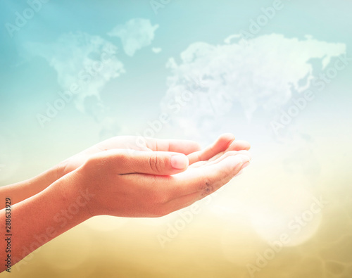Praying hands on world map of clouds background