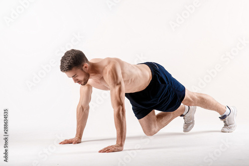 young man with a beard of a sports physique doing push-ups from the floor on a white isolated background, sportsman goes in for sports