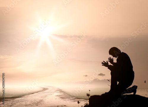 Pray concept: Humble man kneeling to praise and worship God on mountain sunset background	