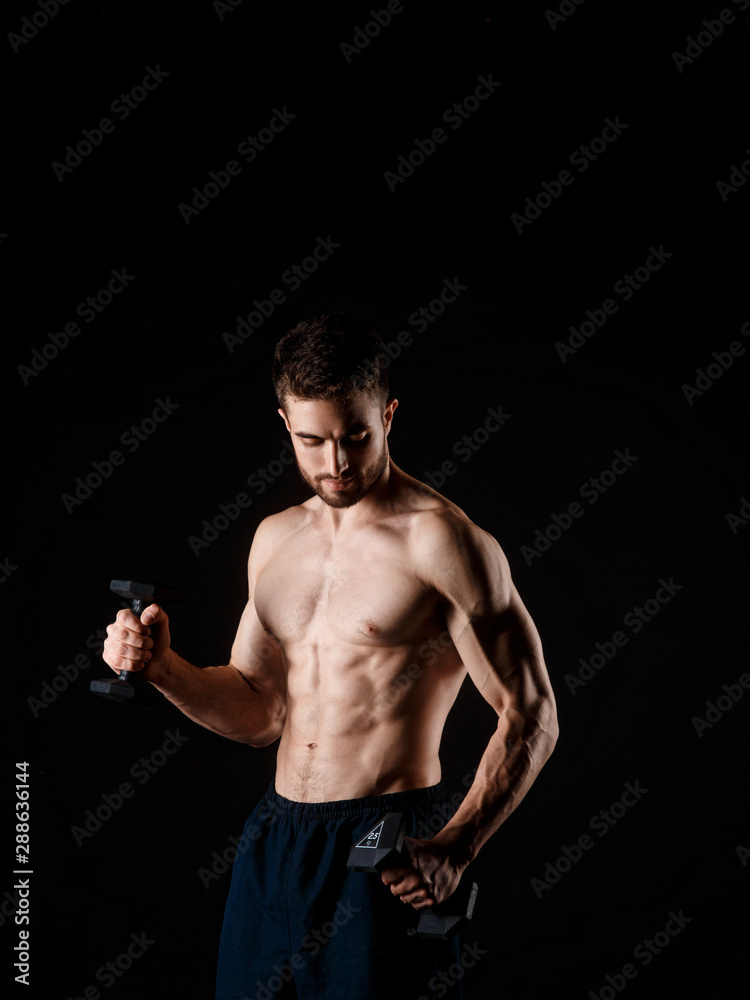 A man on a black background with dumbbells in his hands. young bearded athlete.