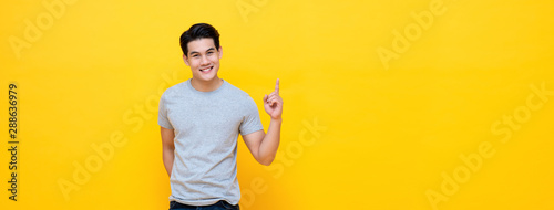 Smiling young handnsome Asian man pointing hand up to copy space aside