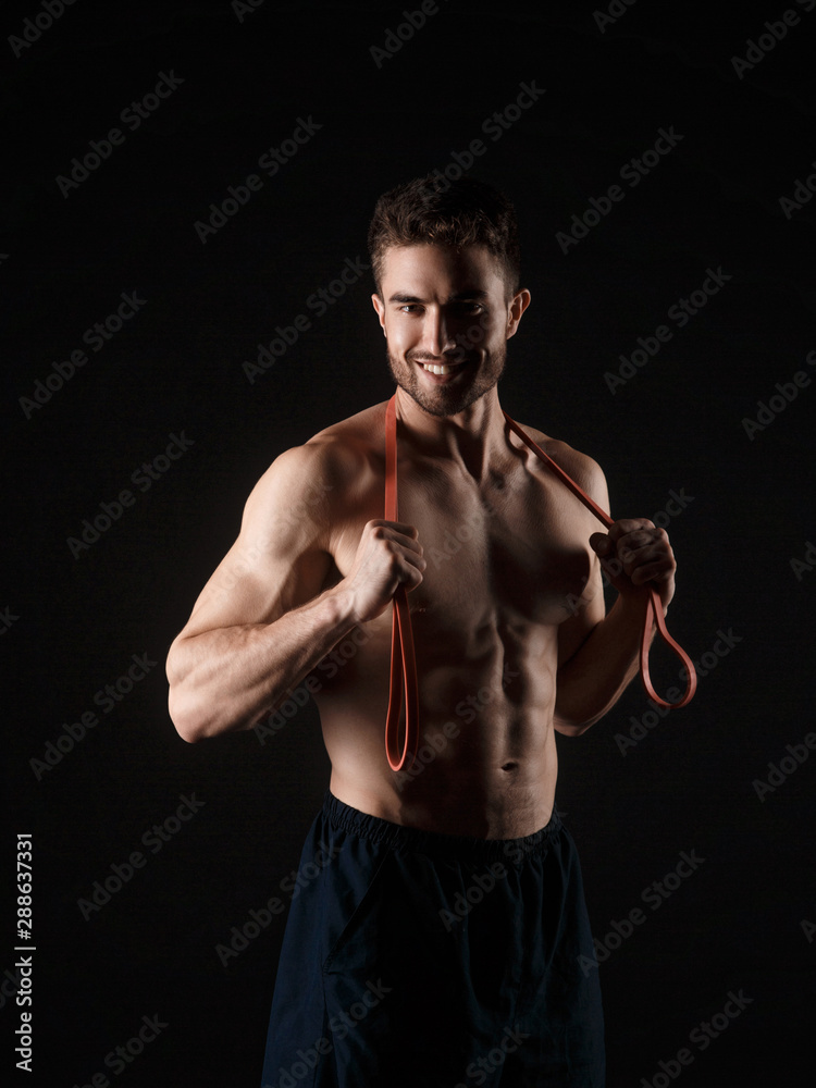 sports man with a beard on a black background with gymnastic elastic bands in hands