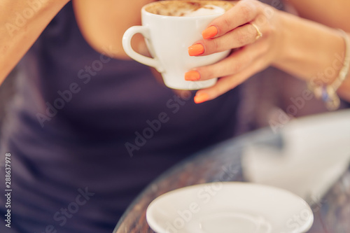 girl's hand holds a cup of cappuccino